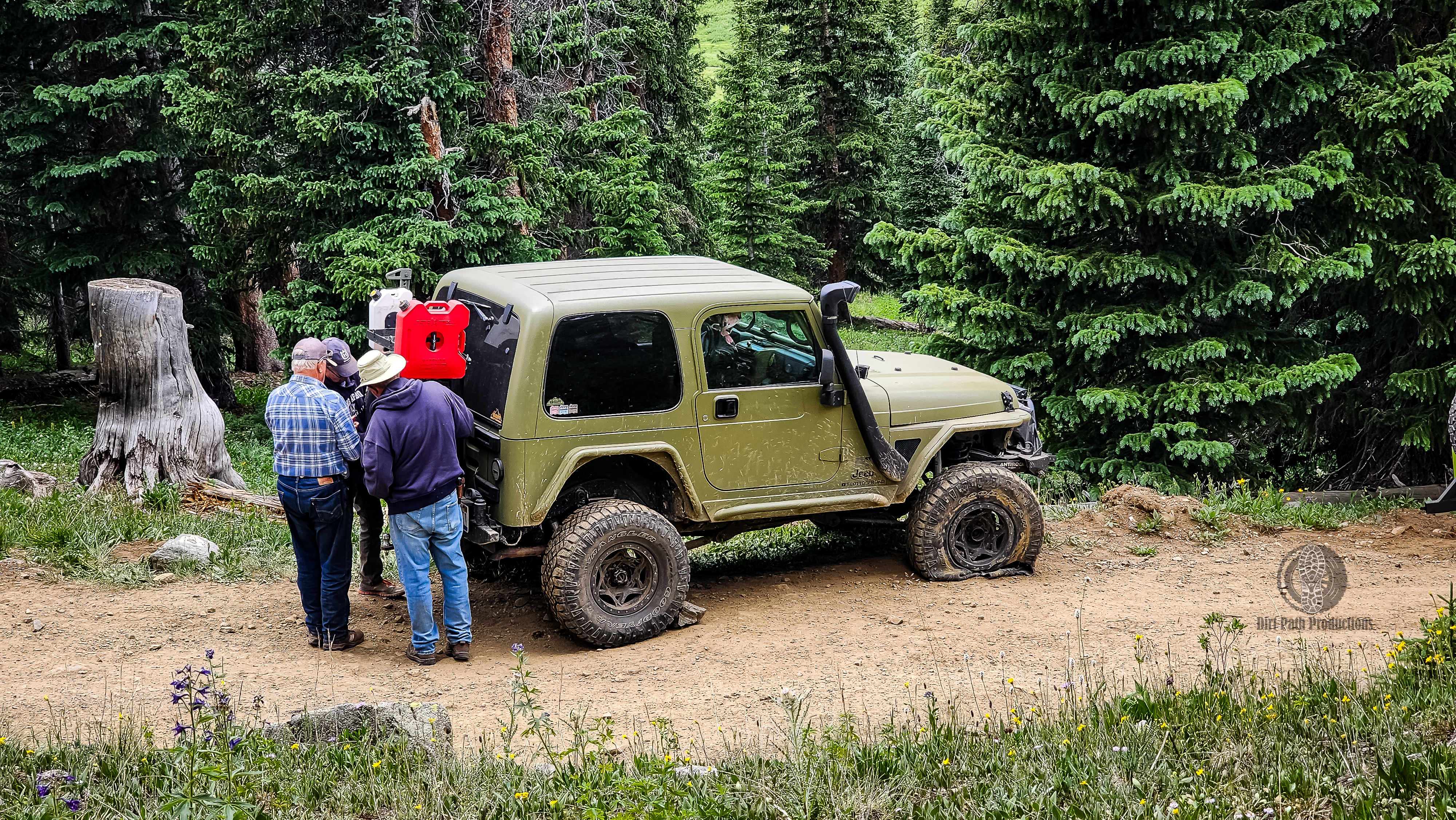 Off-road community coming together to help fix a flat tire on a green Jeep on the trail in Colorado