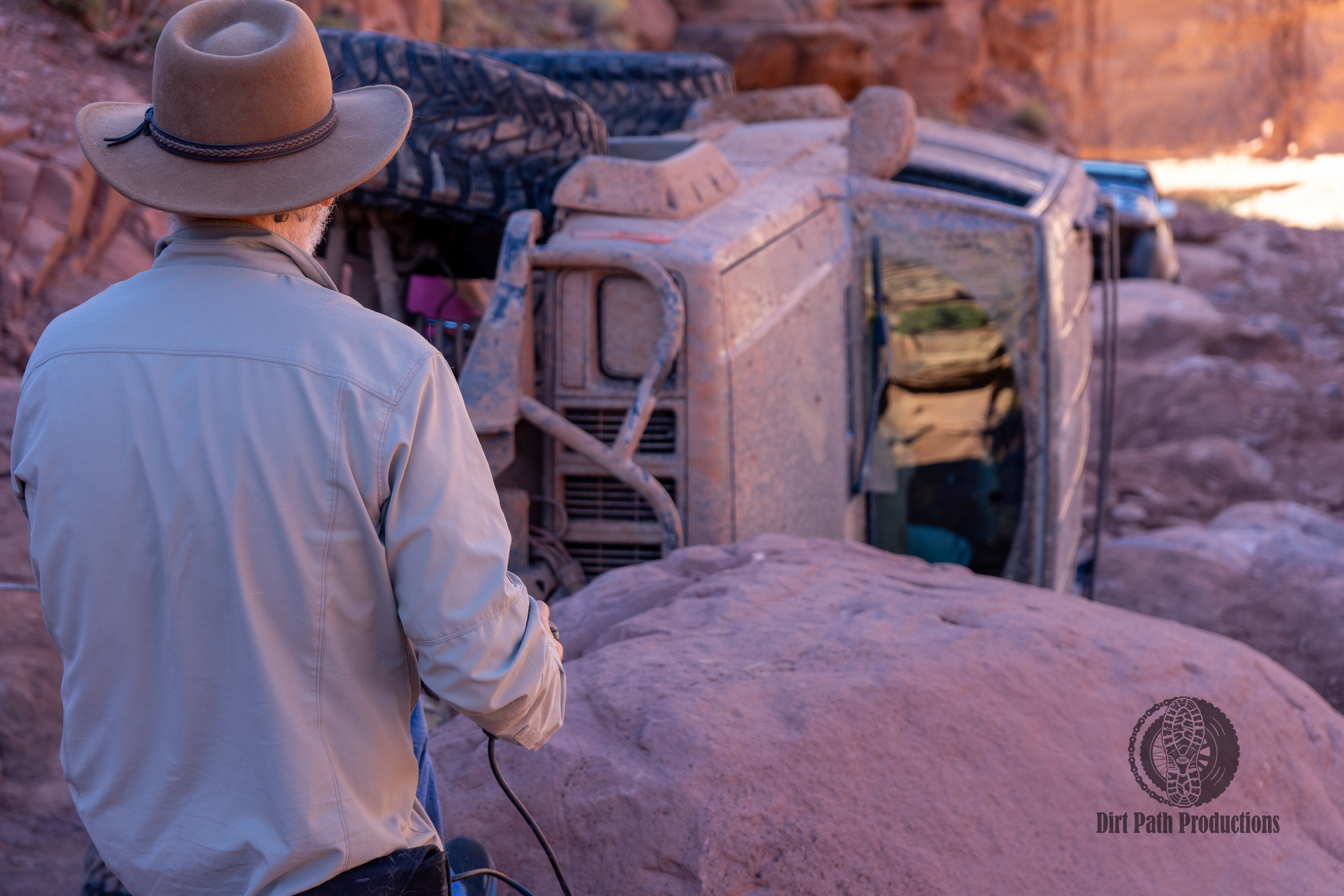 Cowboy looking at a rolled Jeep on desert rocks