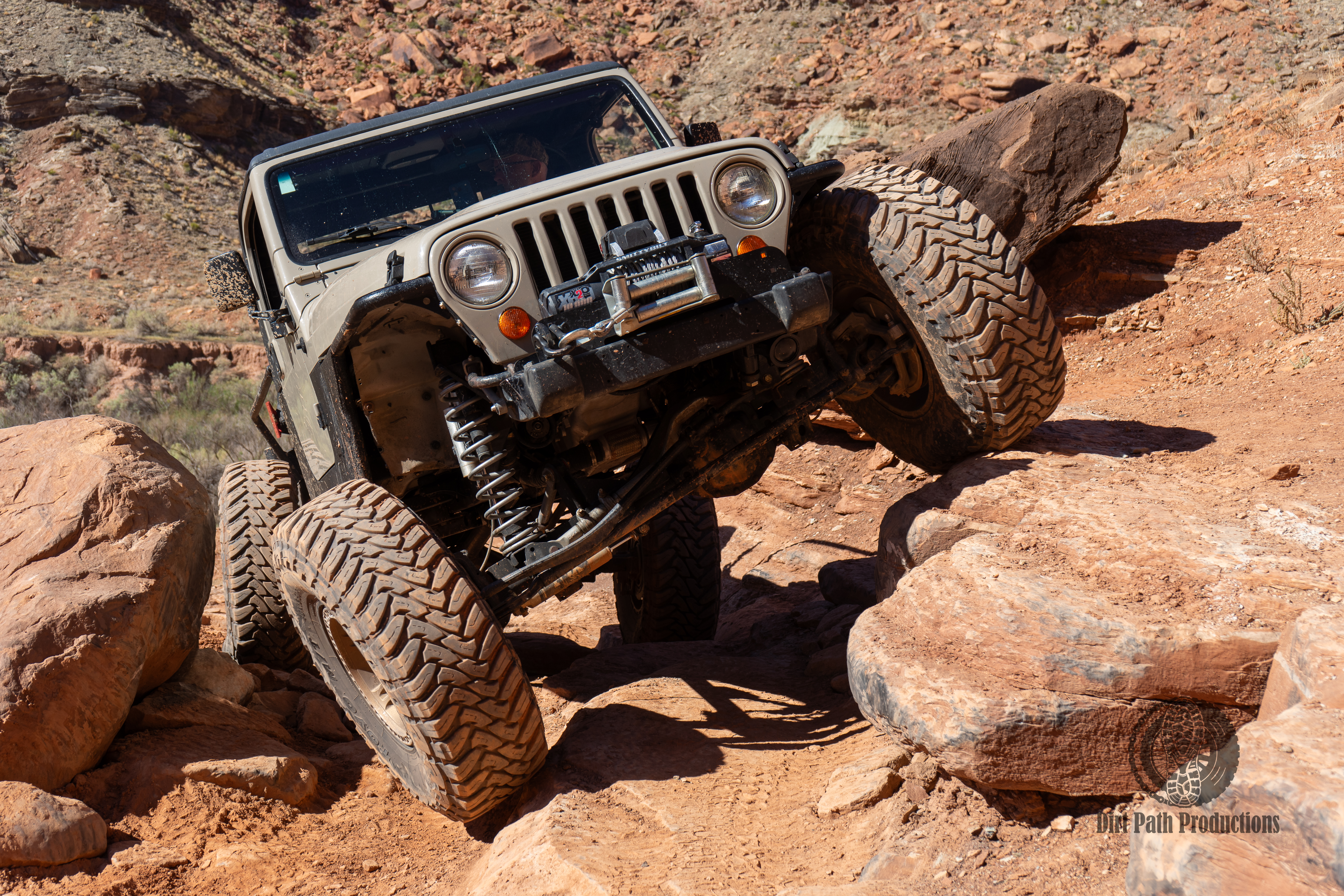 Tan Jeep rock-crawling over boulders in red rock terrain